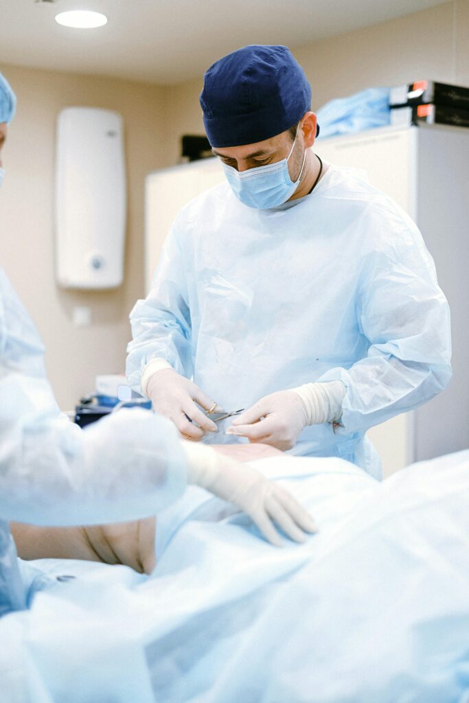 Cirujano con bata, mascarilla y gorro azul utilizando instrumental médico durante una operación.