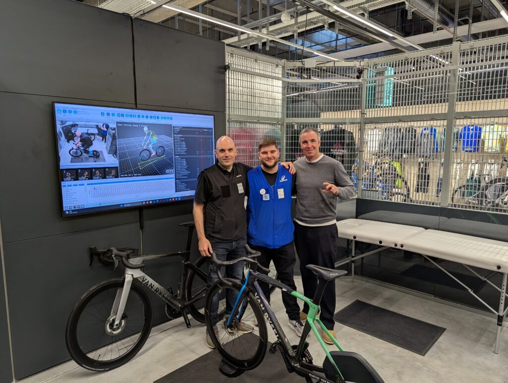 Tres hombres posando juntos frente a la pantalla de análisis en el Van Rysel Bike Fitting Lab.