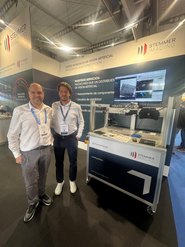 Jorge Molina (STT Systems) e Iker Urdangarin posando en el stand de STEMMER IMAGING durante Advanced Factories 2026, con un sistema de visión artificial de demostración detrás.